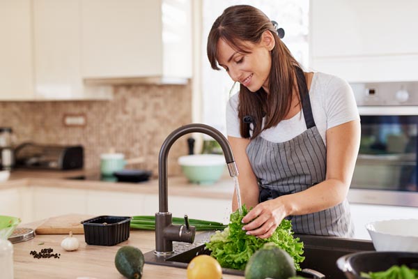 Eine Frau wäscht an einem Becken einen Salat - Küchenhygiene